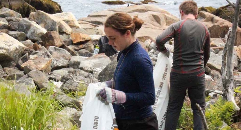 two teens pick up trash along a rocky shoreline during a service project with outward bound in maine